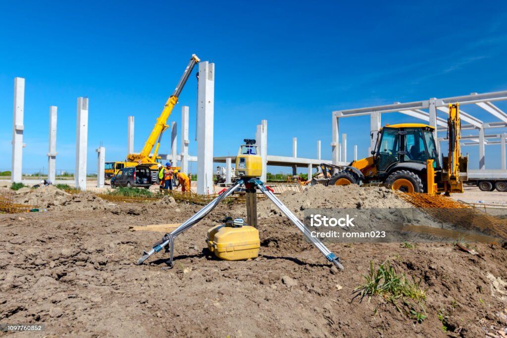 Surveyor instrument for measuring level on construction site, excavator is in background.